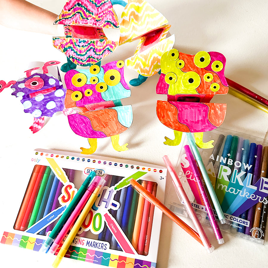 Colorful paper monsters with markers and art supplies on table