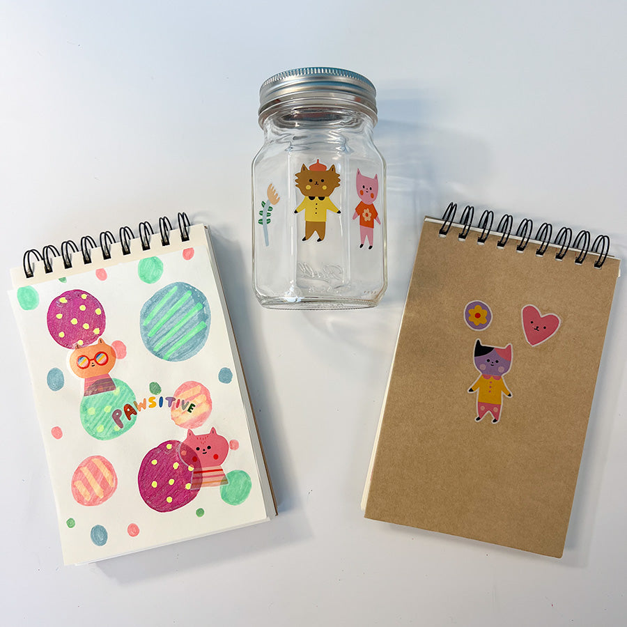 A mason jar, sketchpad cover and sketchpad page with creative colored circles each with a Cat temporary tattoo from OOLY to decorate them.