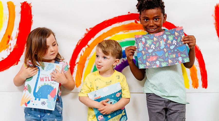 3 kids standing against rainbow painting holding OOLY supplies