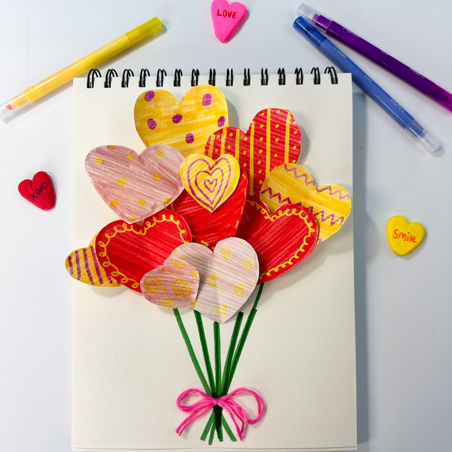 A collection of heart-shaped cutouts placed beside the White DIY Cover Sketchbook. 