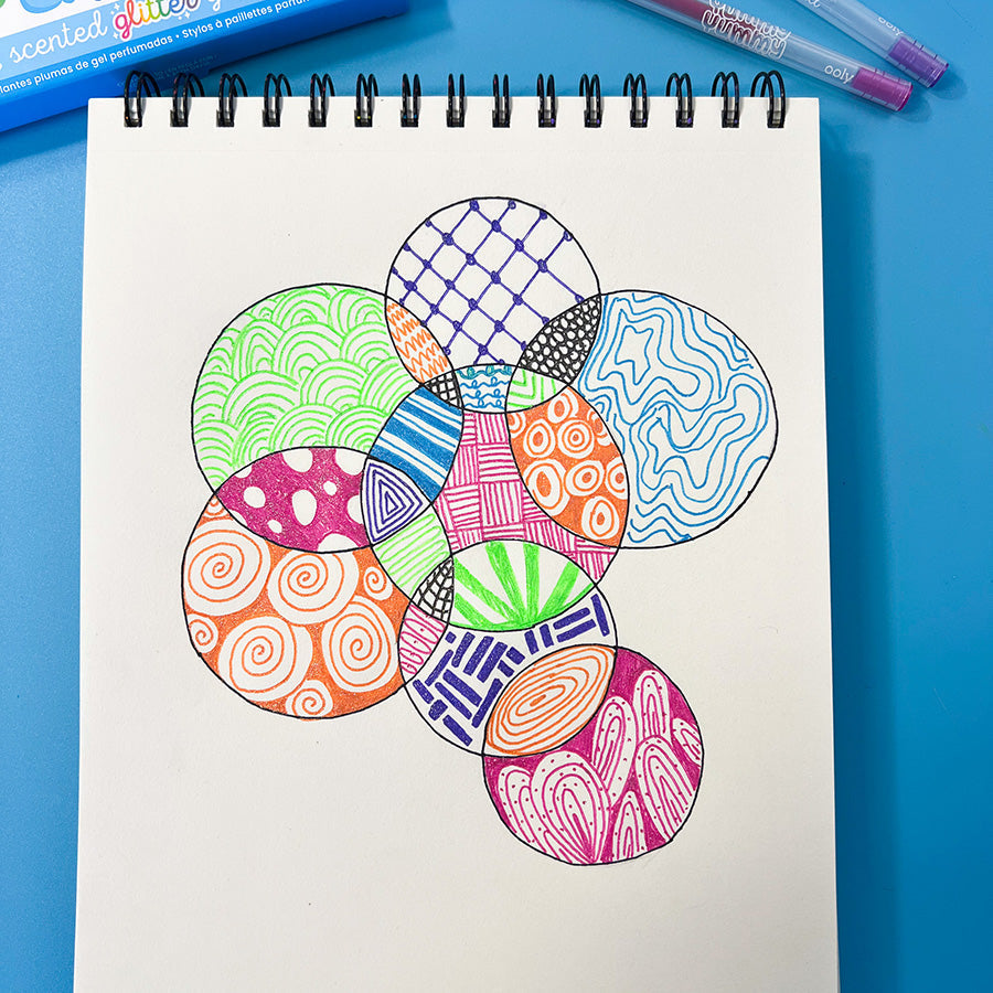 A completed zentangle artwork with every section of the overlapping circles filled with vibrant, glittery patterns like waves, checkerboards, and spirals, using Yummy Yummy Scented Glitter Gel Pens.