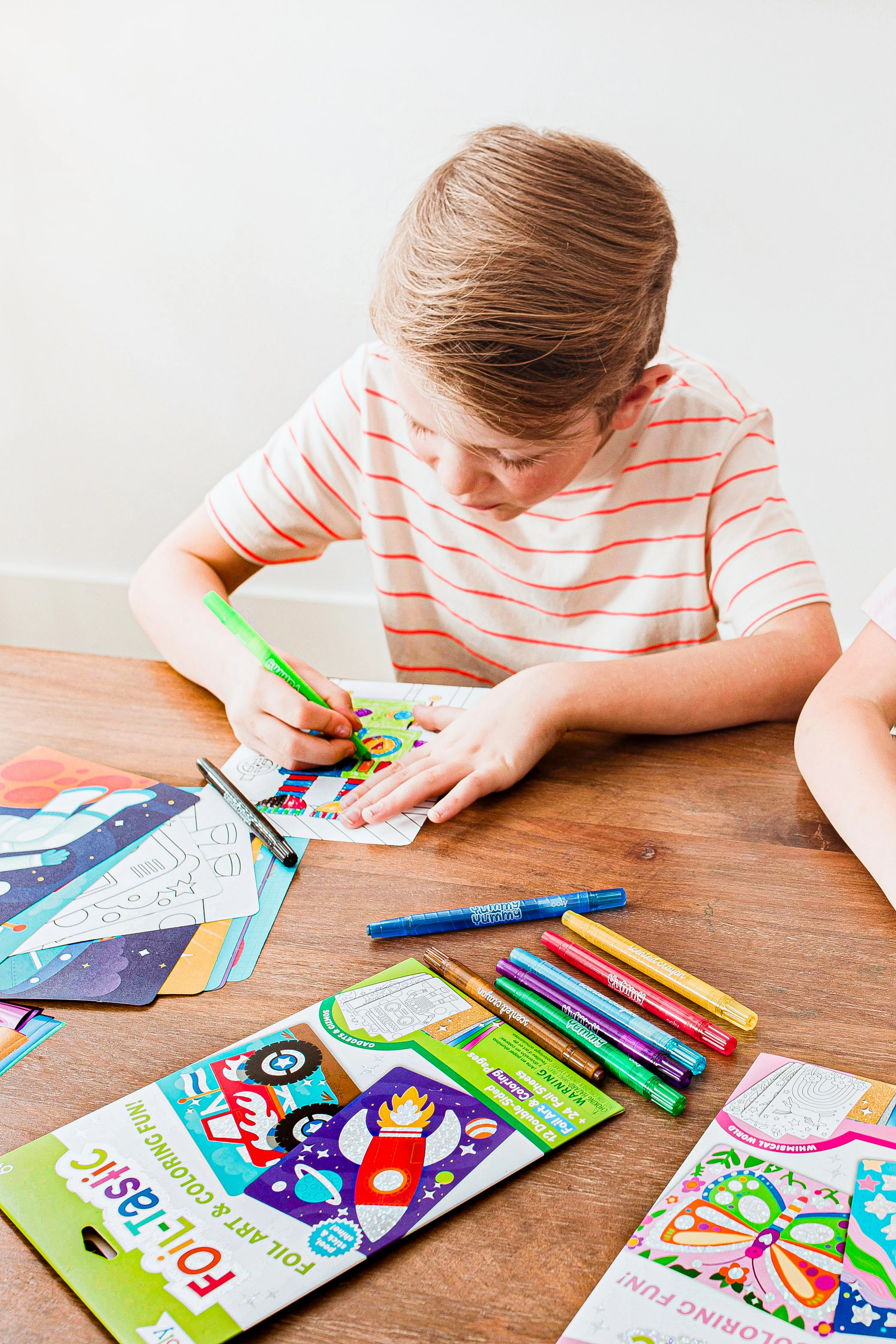 Boy coloring in OOLY Foil-Tastic Foil Art Coloring Set with crayons on wooden table