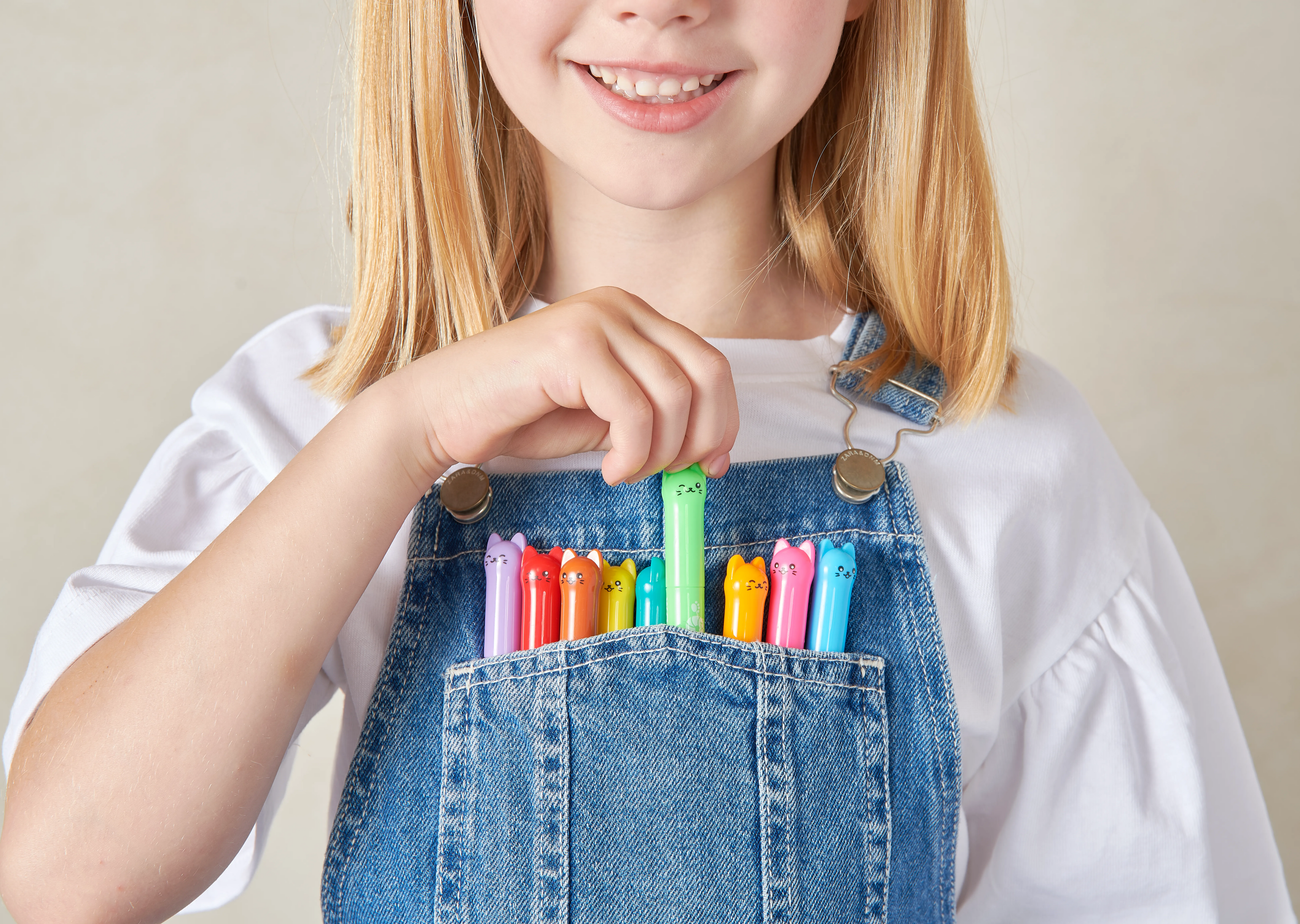 Close up of girl with collection of OOLY Cat Parade Gel Crayons in her overalls pocket