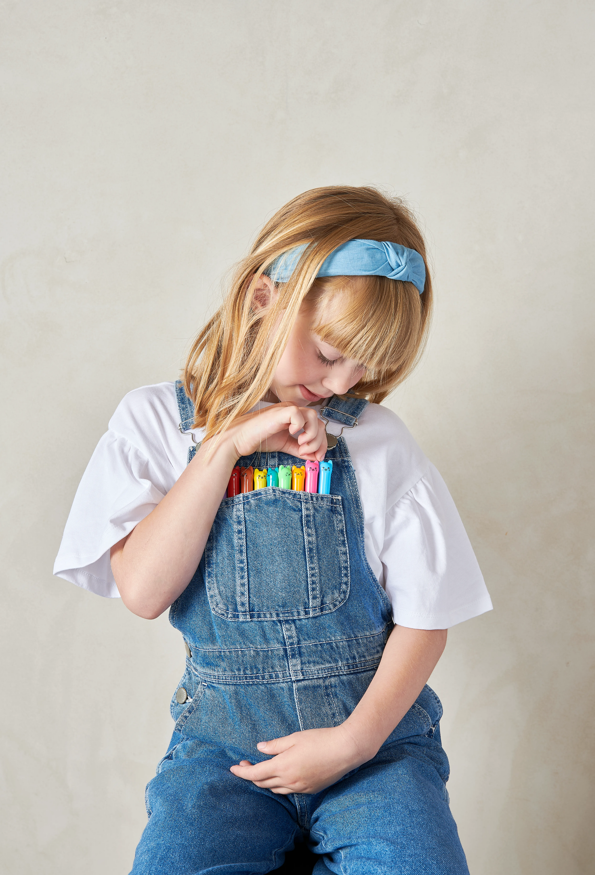 Girl with collection of OOLY Cat Parade Gel Crayons in her overalls pocket