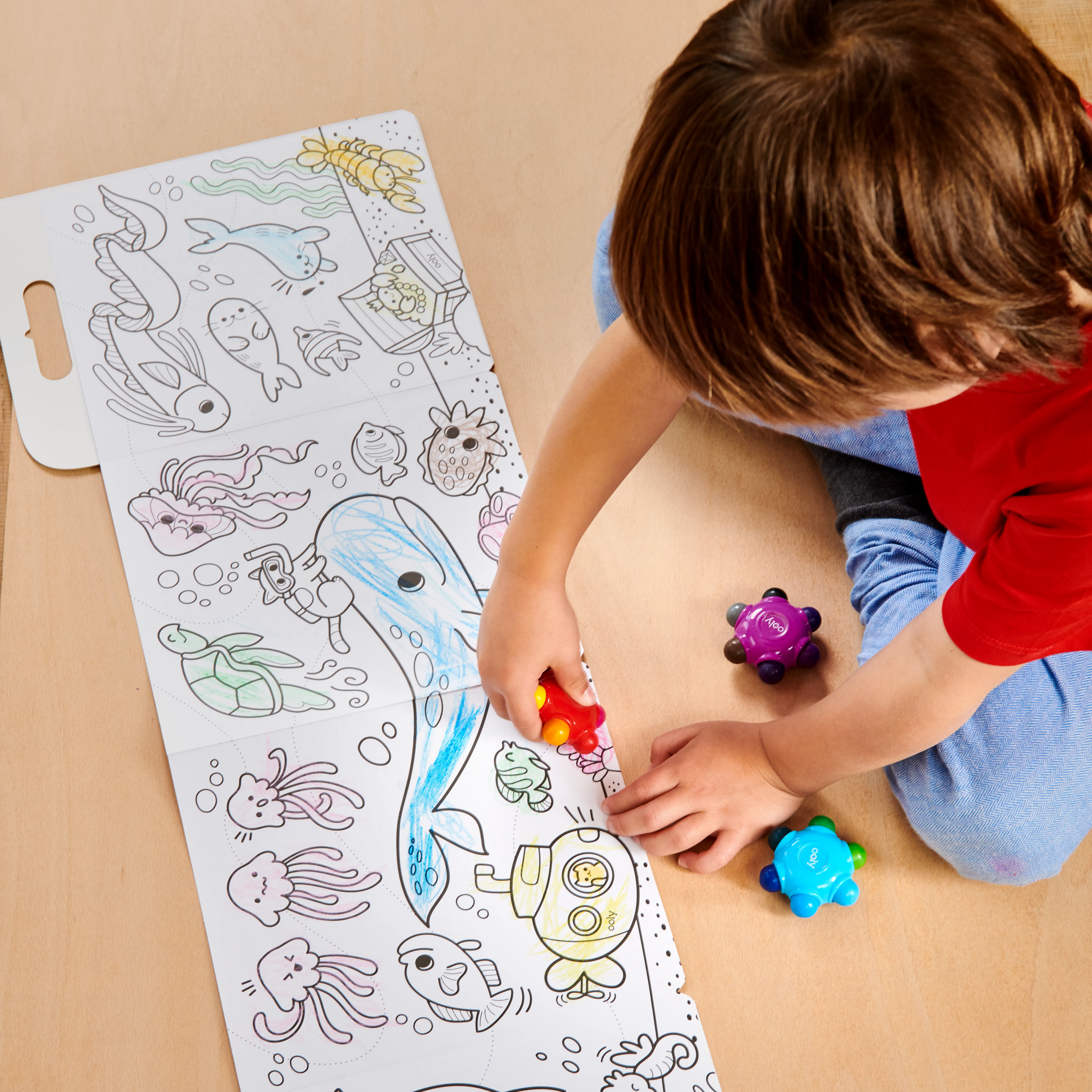 Boy coloring sea animal coloring book with set of OOLY Color Burst Crayons