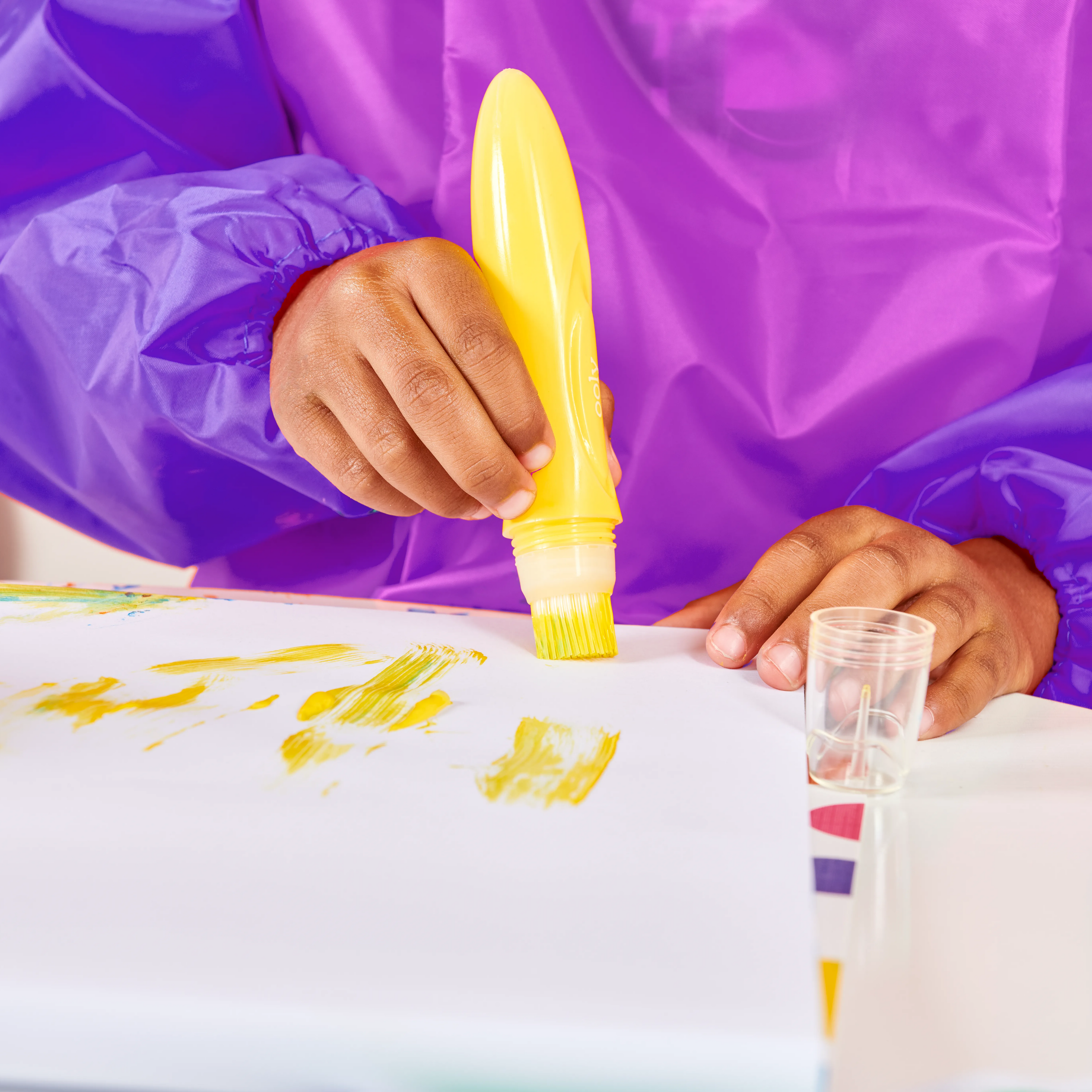 Close up of kid dressed in purple painting with a yellow paint brush from OOLY Easy Squeezy Squeezable Poster Paint Brushes