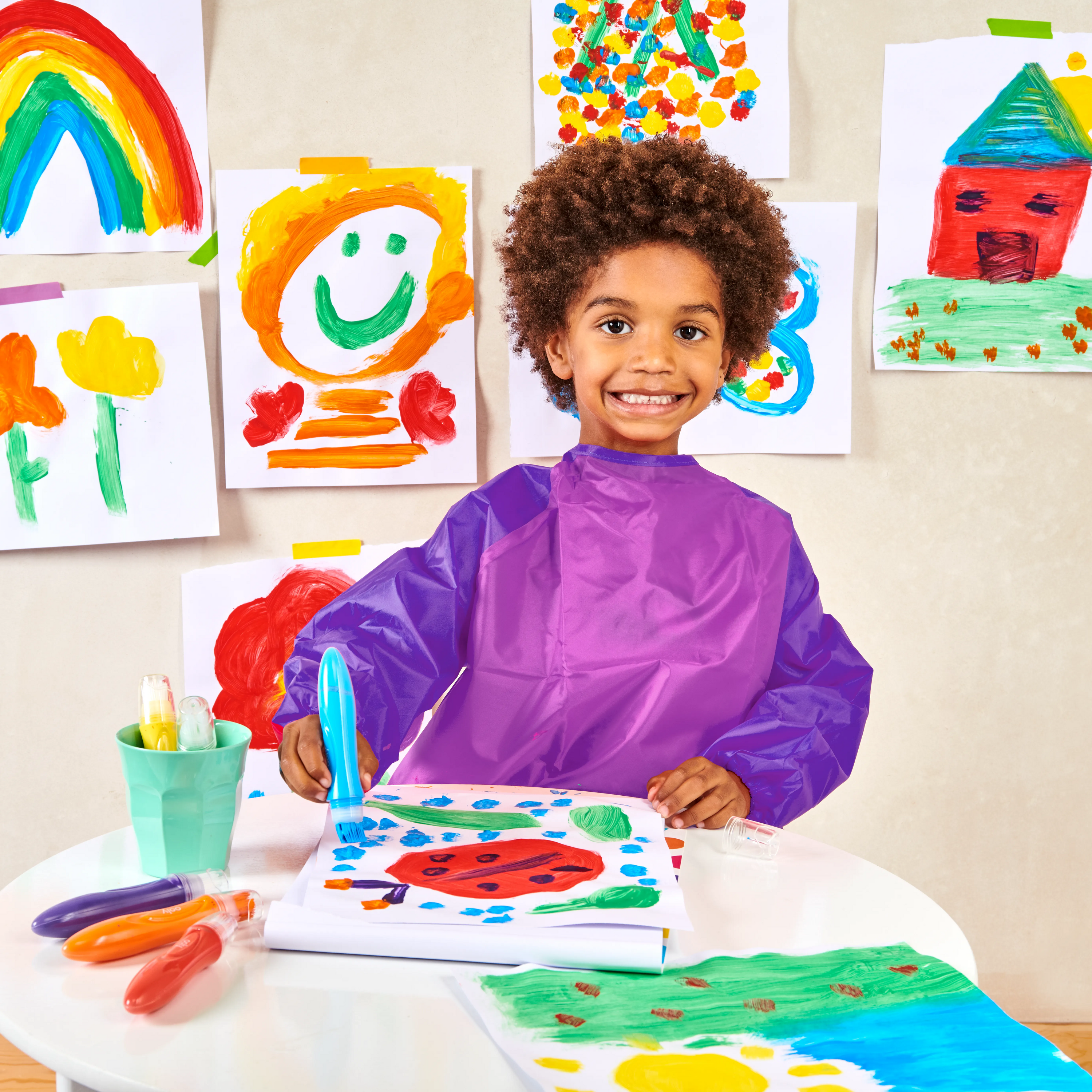 Kid smiling while painting with a blue paint brush from OOLY Easy Squeezy Squeezable Poster Paint Brushes