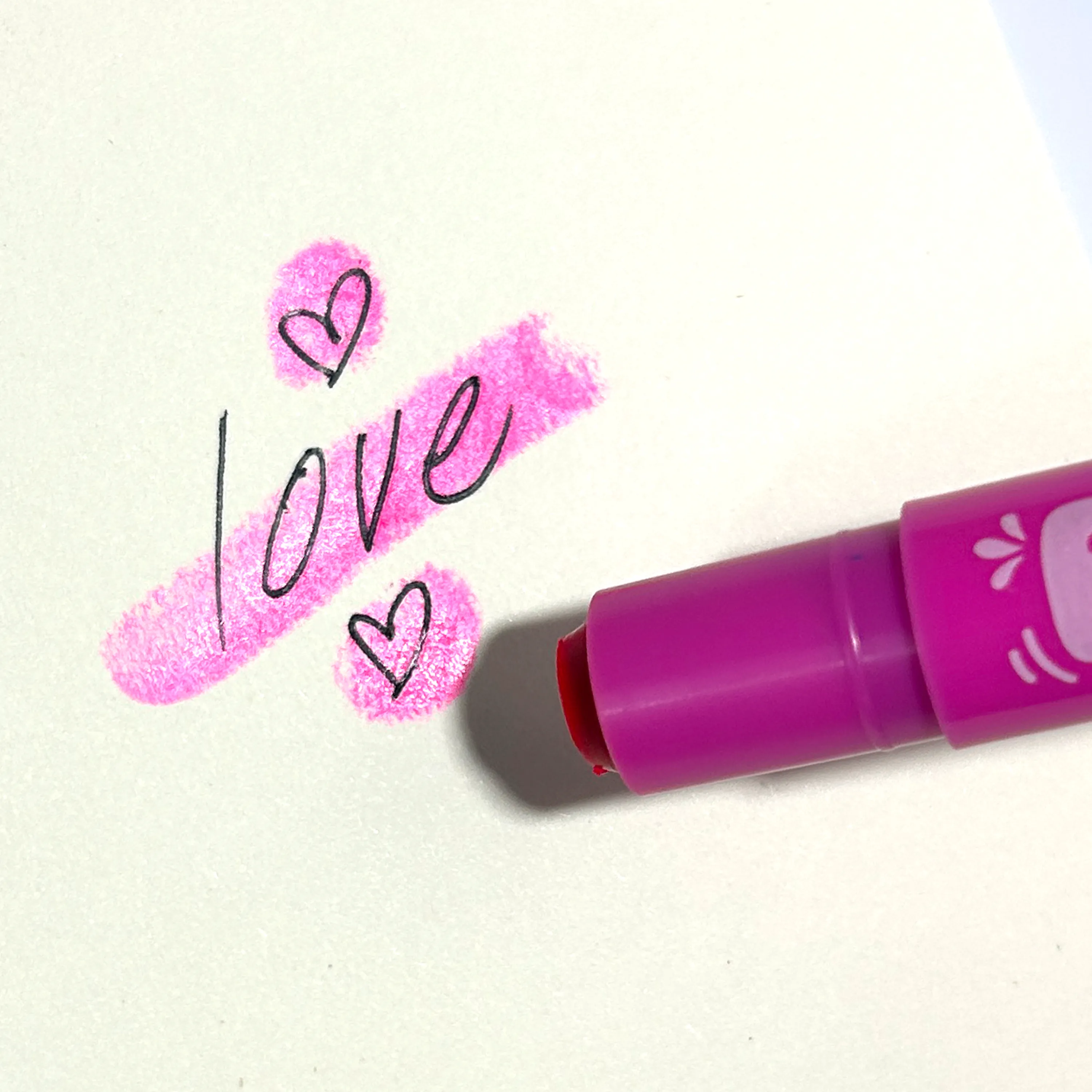 Close up of "Love" written with hearts on sketchbook highlighted with a pink OOLY Fresh Pick Apple Scented Gel Crayon