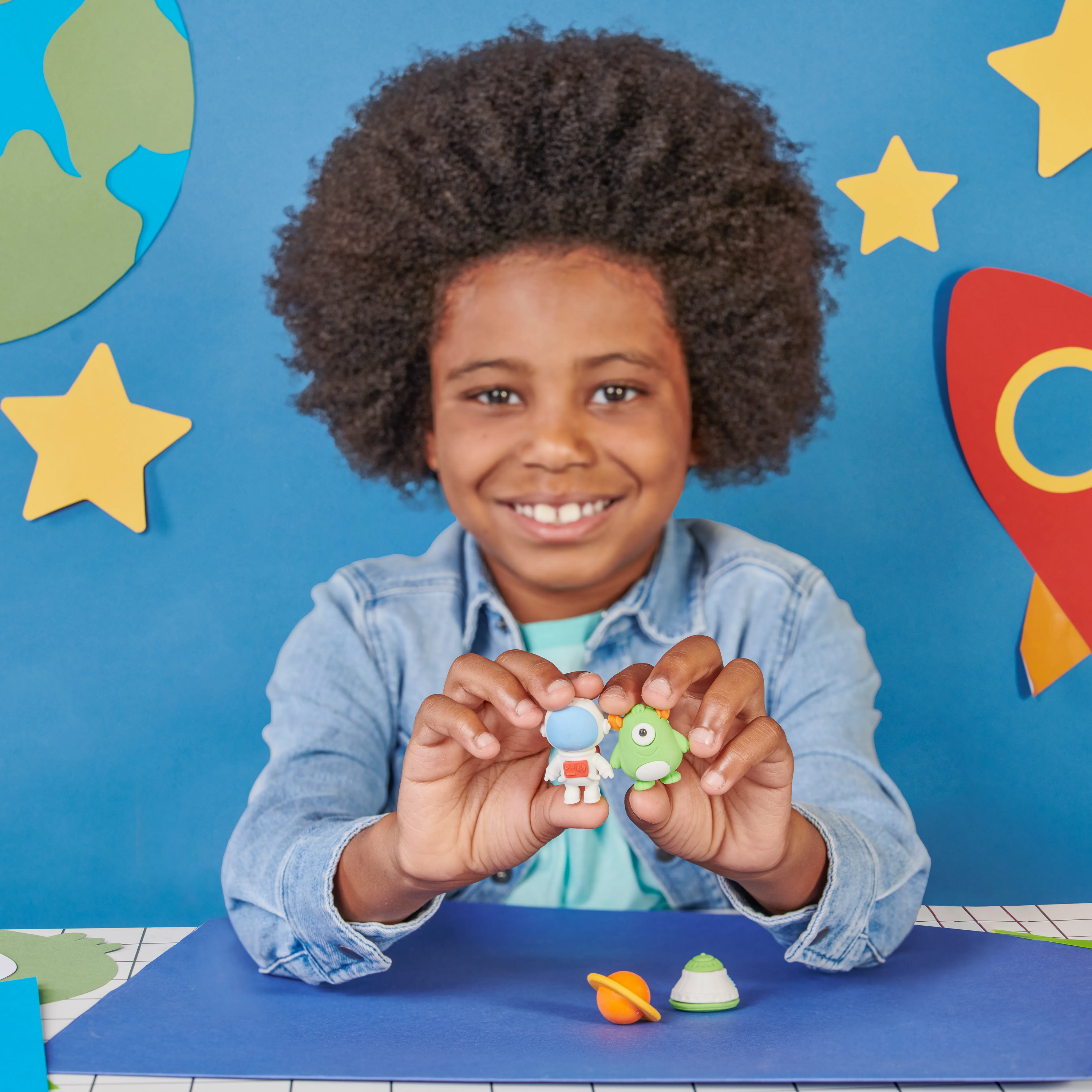 Kid in blue space themed background holding erasers from OOLY Outta This World Scented Puzzle Erasers