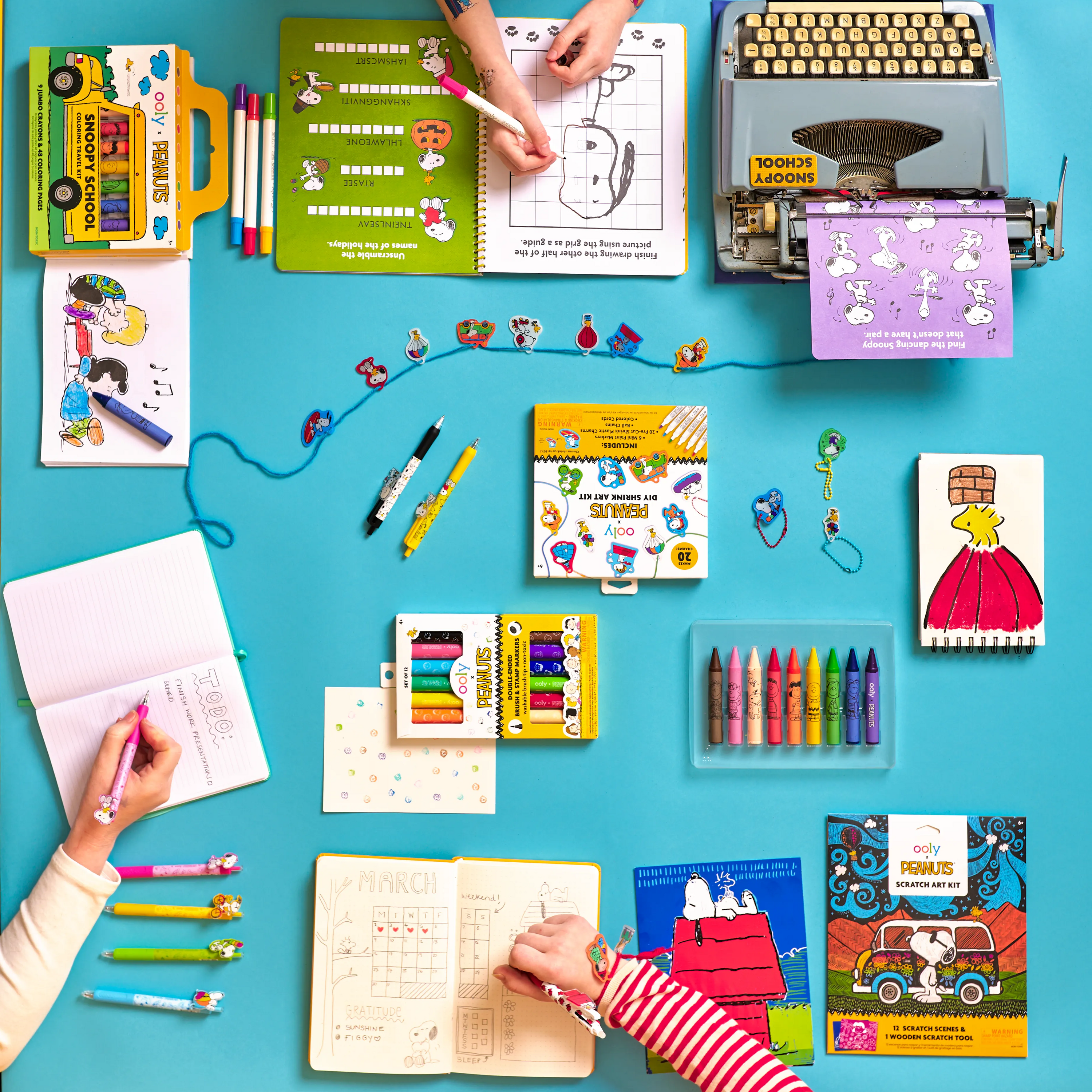 Blue table top with OOLY and Peanuts products including crayons, stamp markers, scratch art kit, a Snoopy activity kit and more.