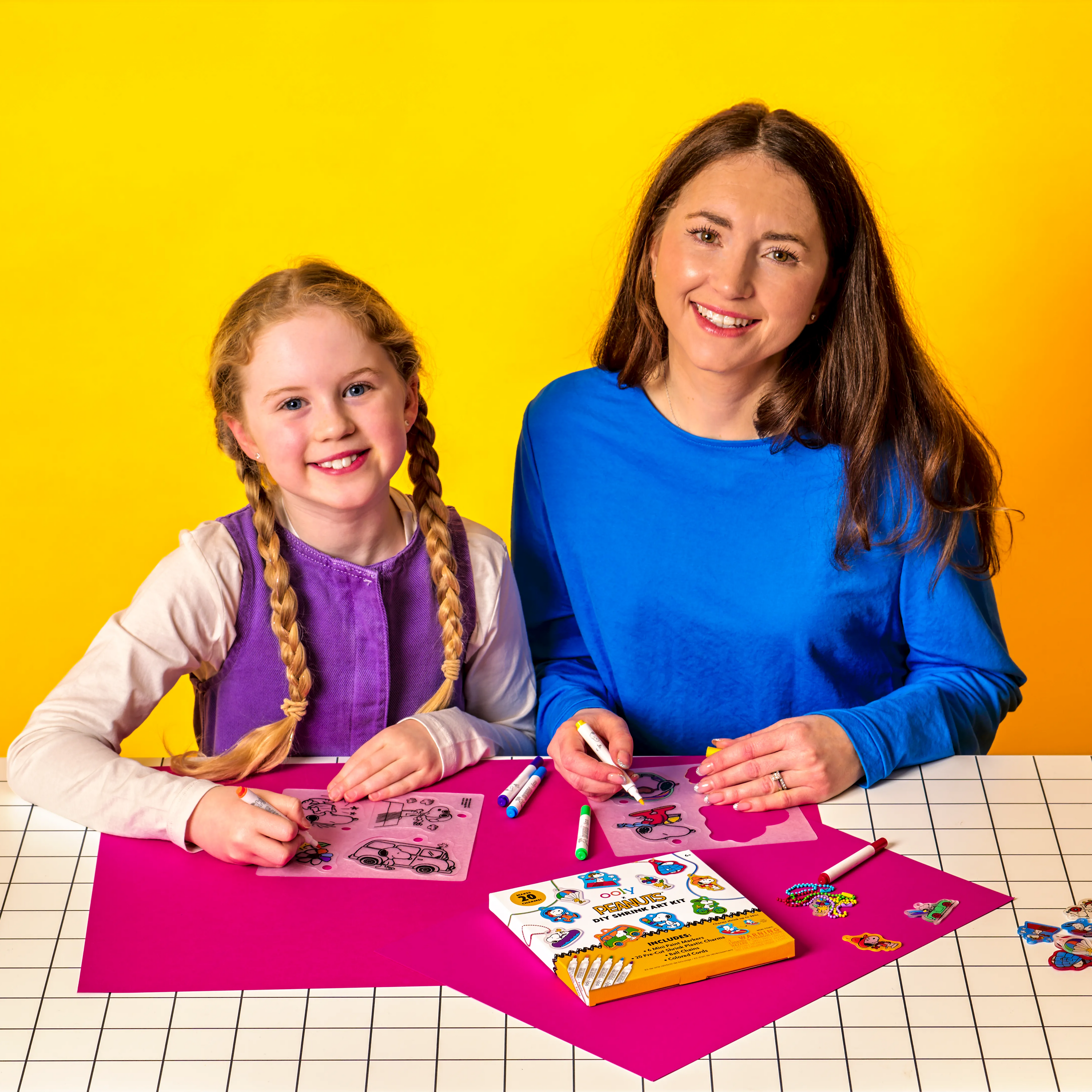 Woman and girl smiling as they color shrink charms from the OOLY x Peanuts DIY Shrink Art Kit