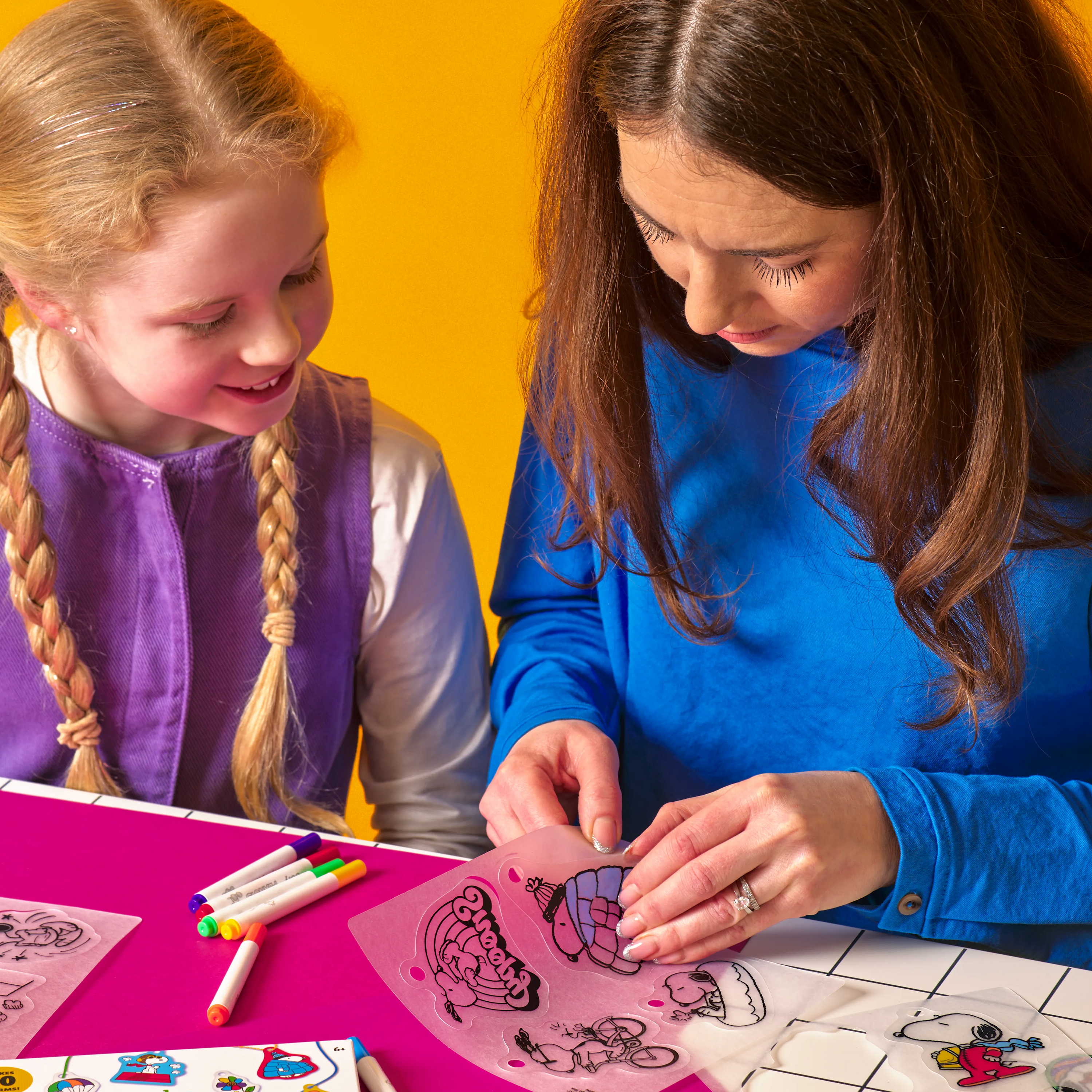 Woman and girl coloring shrink charms from the OOLY x Peanuts DIY Shrink Art Kit