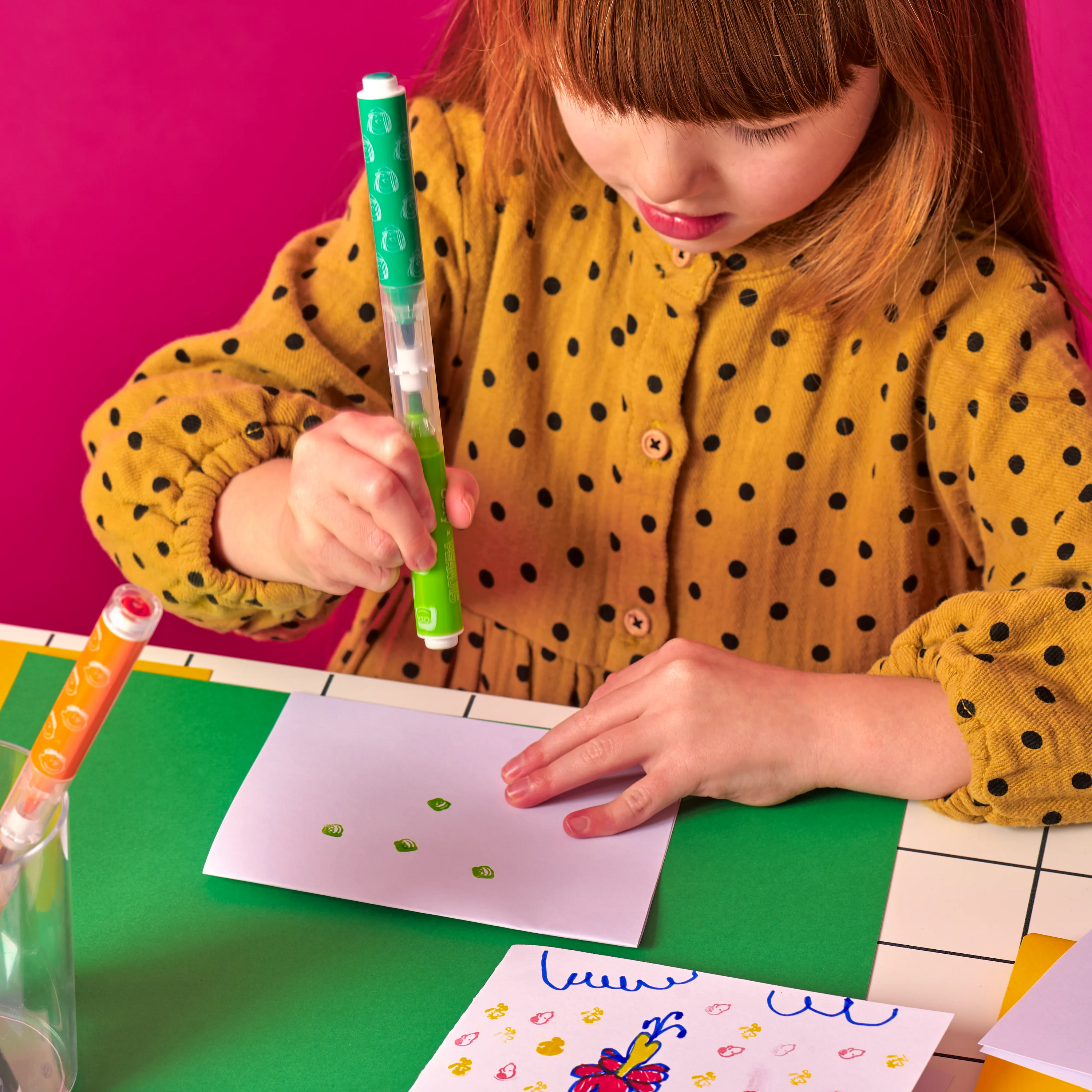 Girl holding green double stamp marker from the OOLY x Peanuts Double-Ended Brush & Stamp Markers set, stamping on white card 