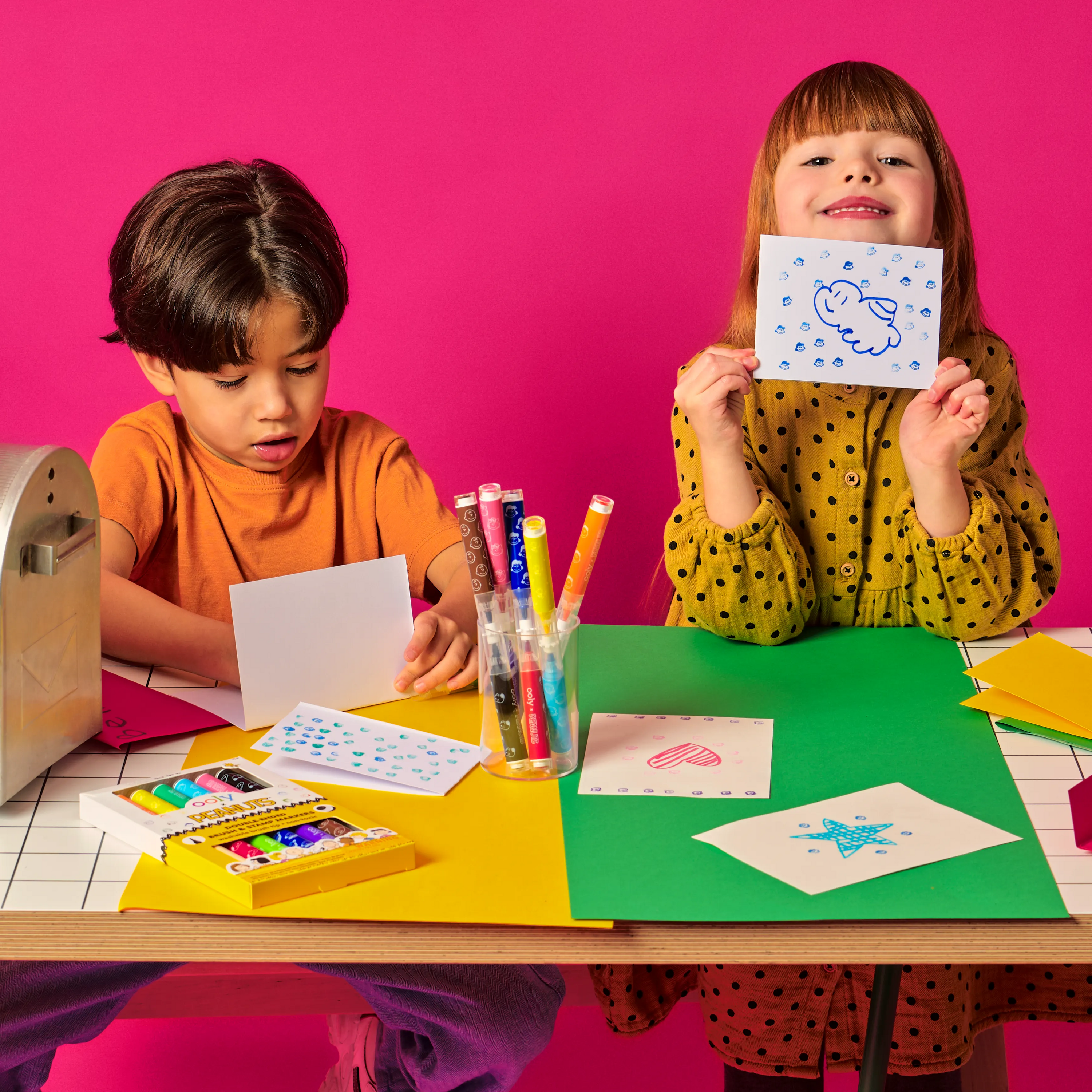 Two kids making stamp creations on paper using OOLY x Peanuts Double-Ended Brush & Stamp Markers