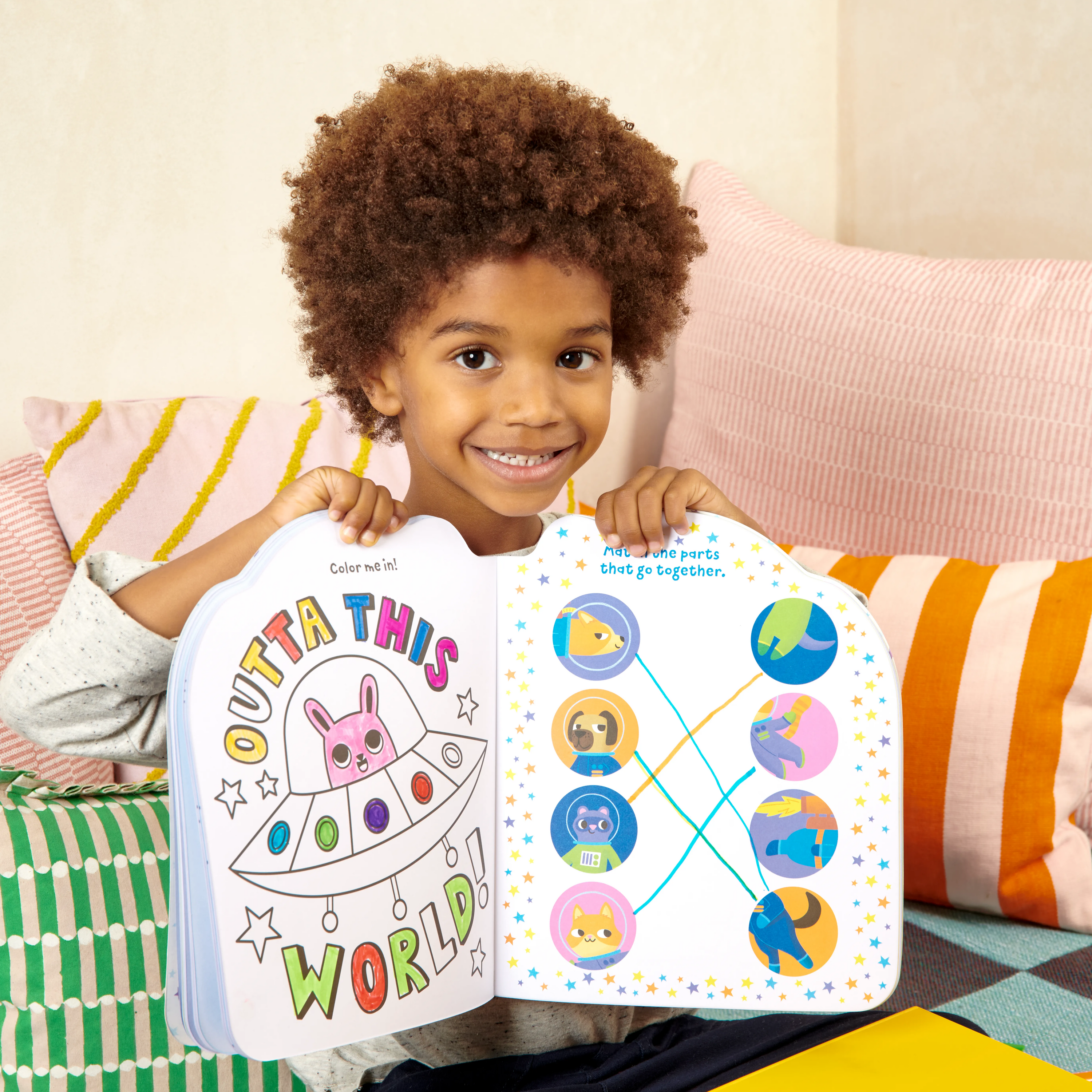 Girl on couch holding open OOLY Playful Pages Activity Book - Games Coloring Stickers - Pets in Space showing coloring and games