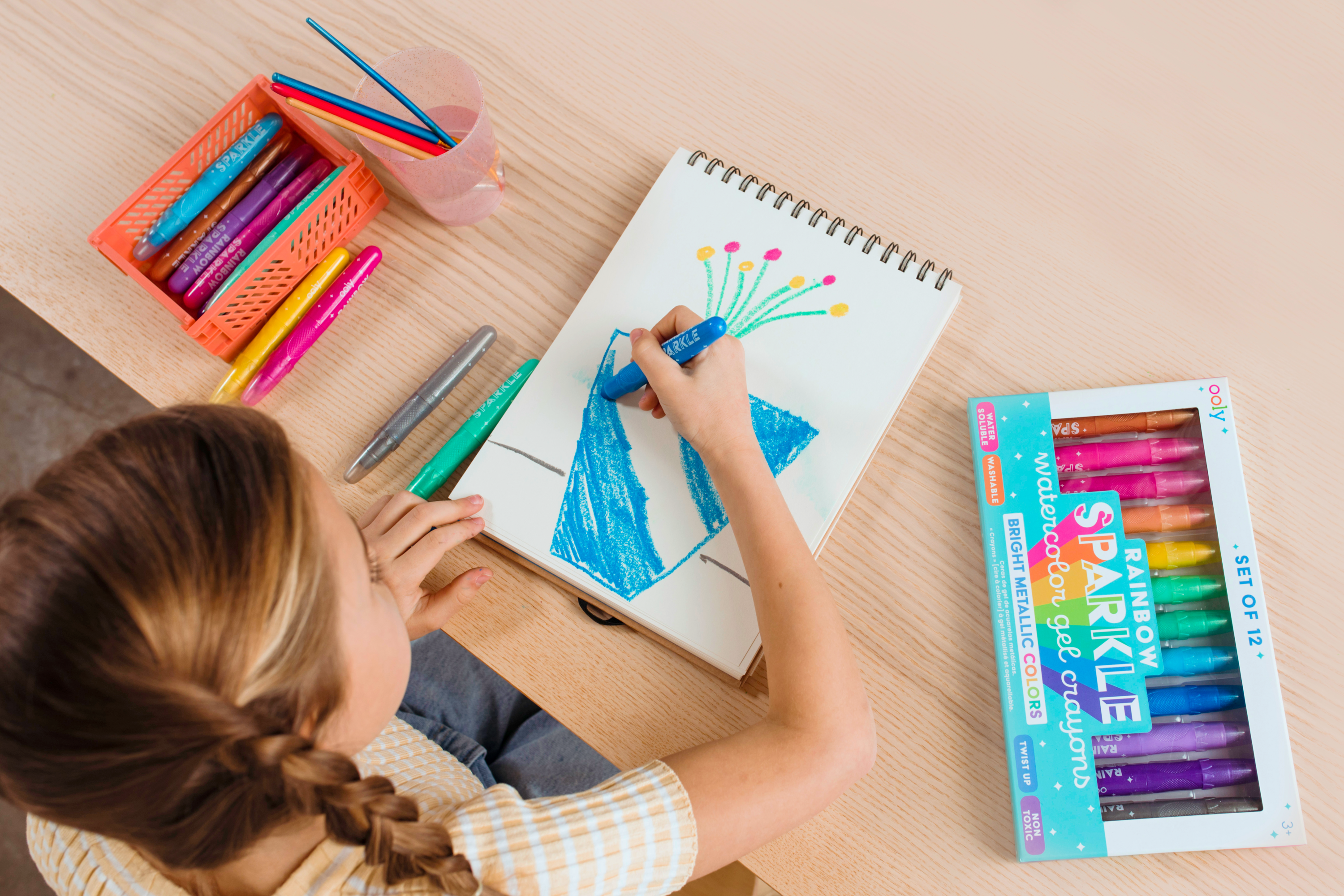 High angle of girl coloring blue flower pot with OOLY Rainbow Sparkle Metallic Watercolor Gel Crayons