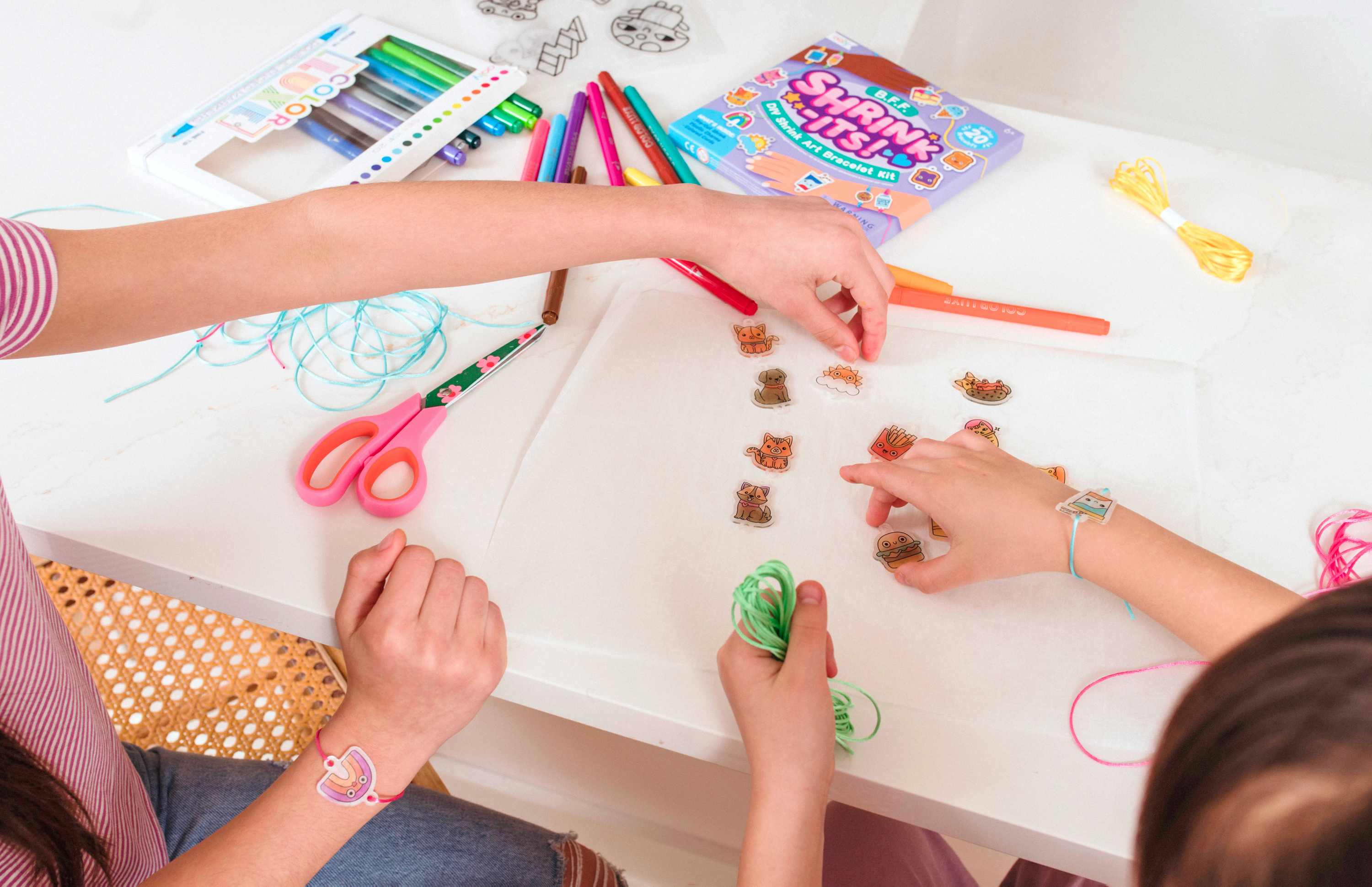 Mom and daughter placing colored charms from OOLY Shrink-its! DIY Shrink Art Bracelet Kit - BFF on sheet