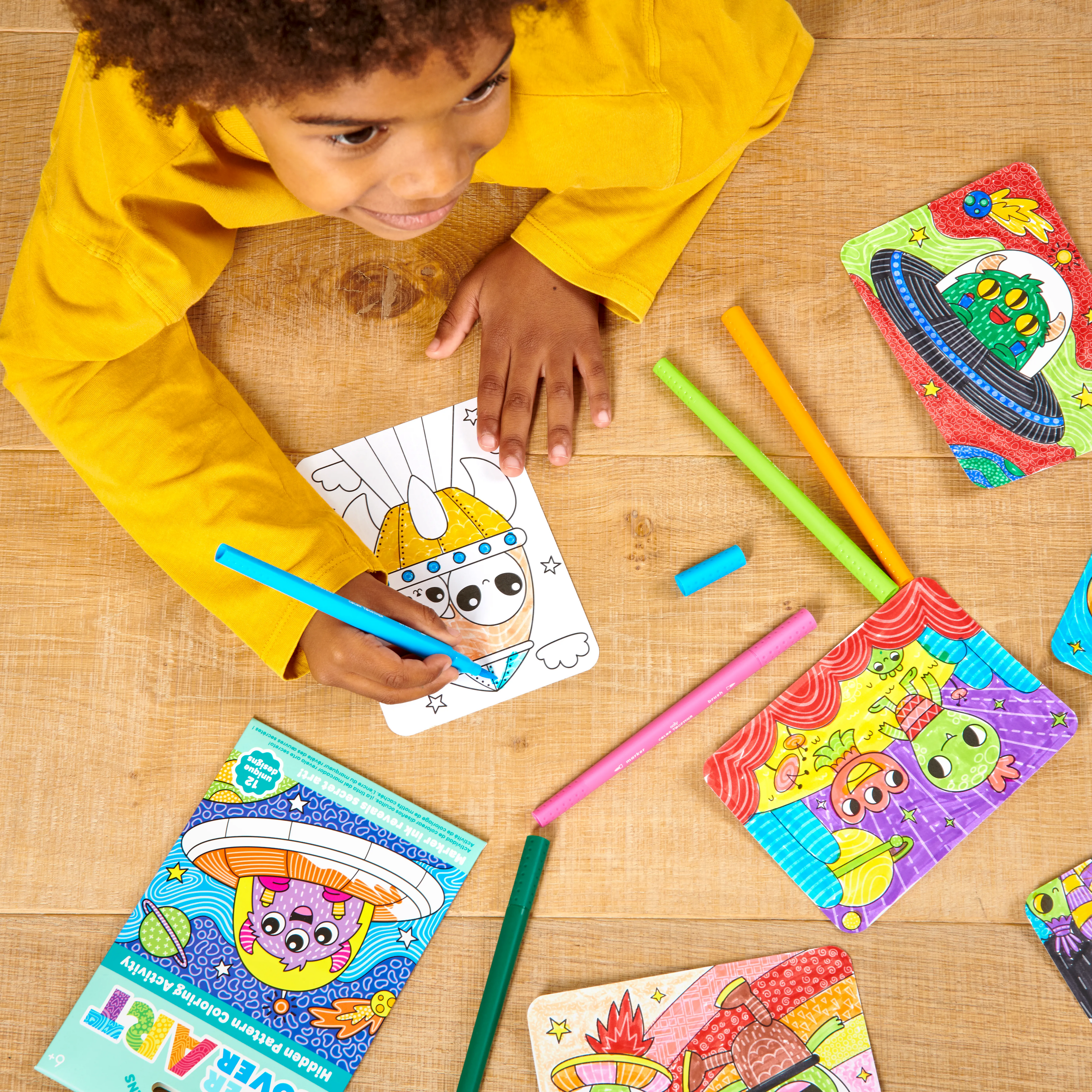 Kid in yellow shirt on wood floor coloring UFO cards from OOLY Undercover Art Hidden Pattern Coloring Activity Art Cards