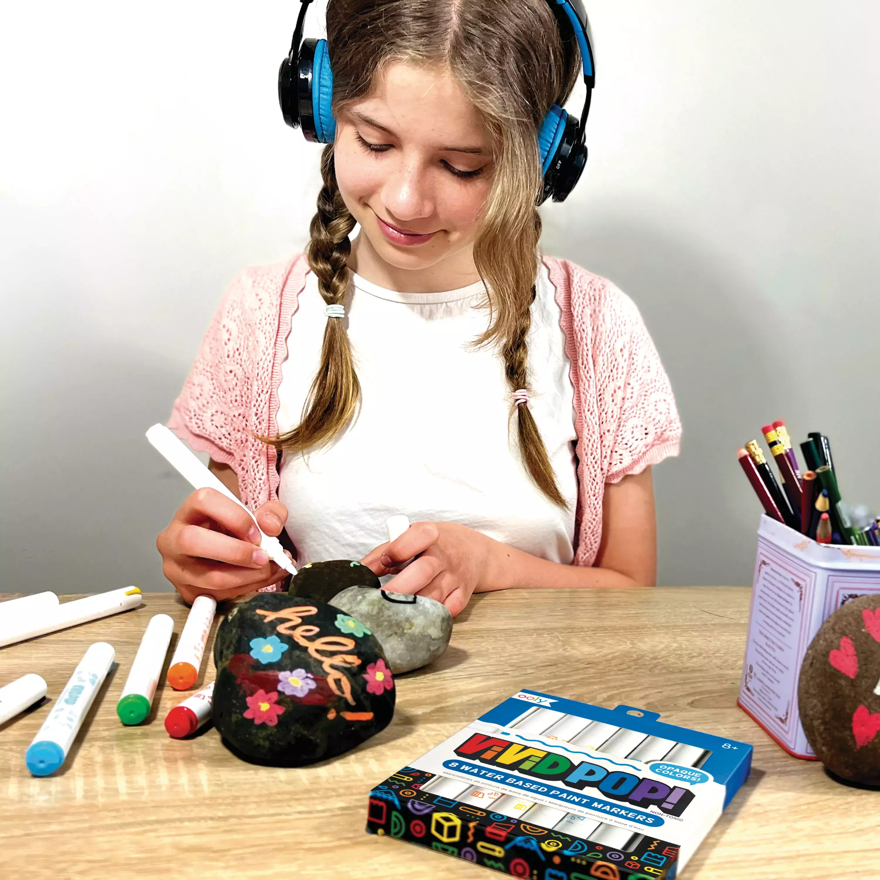 Girl painting rocks with OOLY Vivid Pop! paint markers on wooden table top
