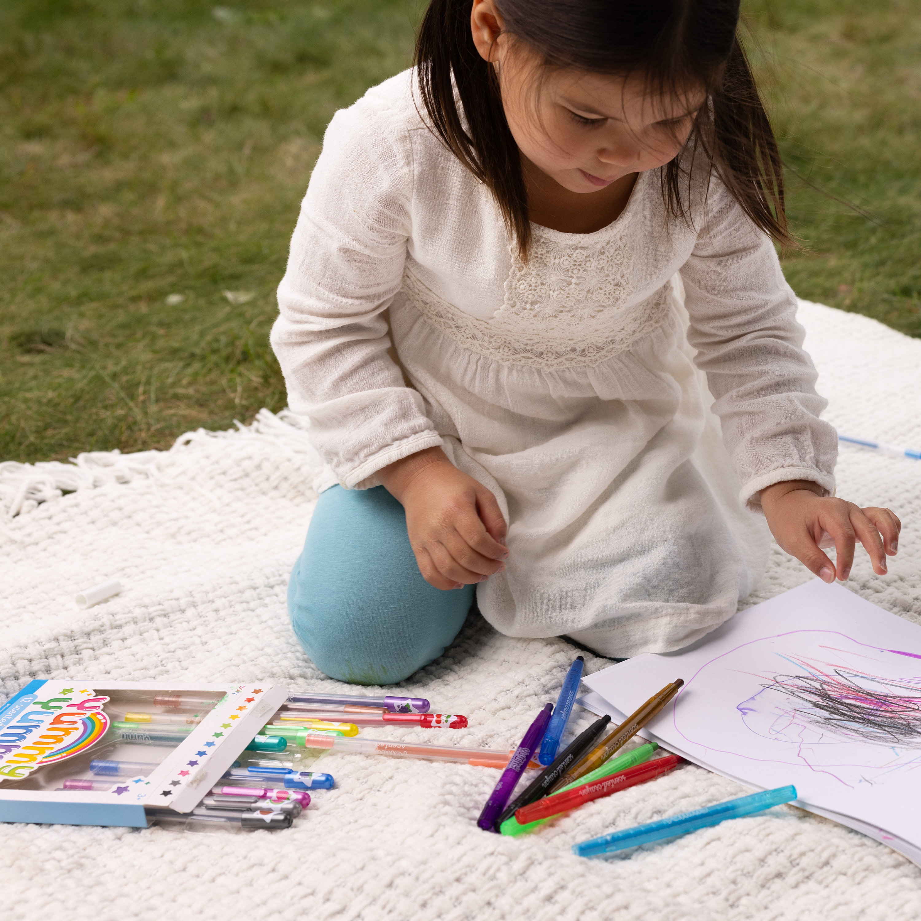 Little girl on a blanket on grass coloring with OOLY Yummy Yummy Scented Glitter Gel Pens